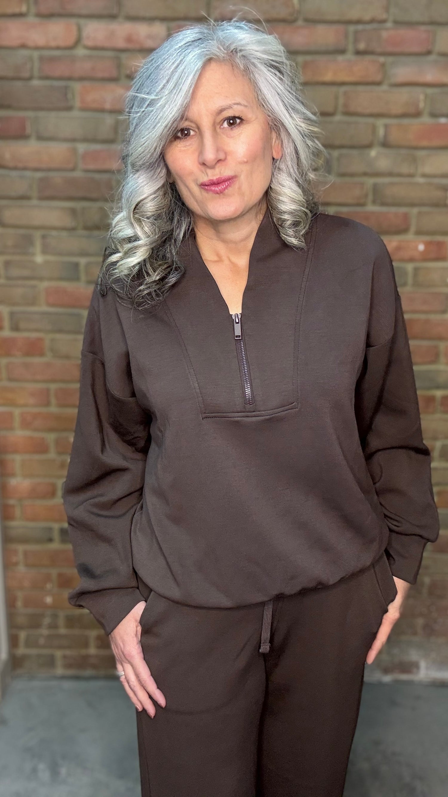 Woman wearing a brown outfit standing against a brick wall.