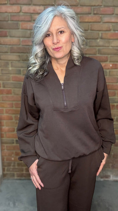 Woman wearing a brown outfit standing against a brick wall.