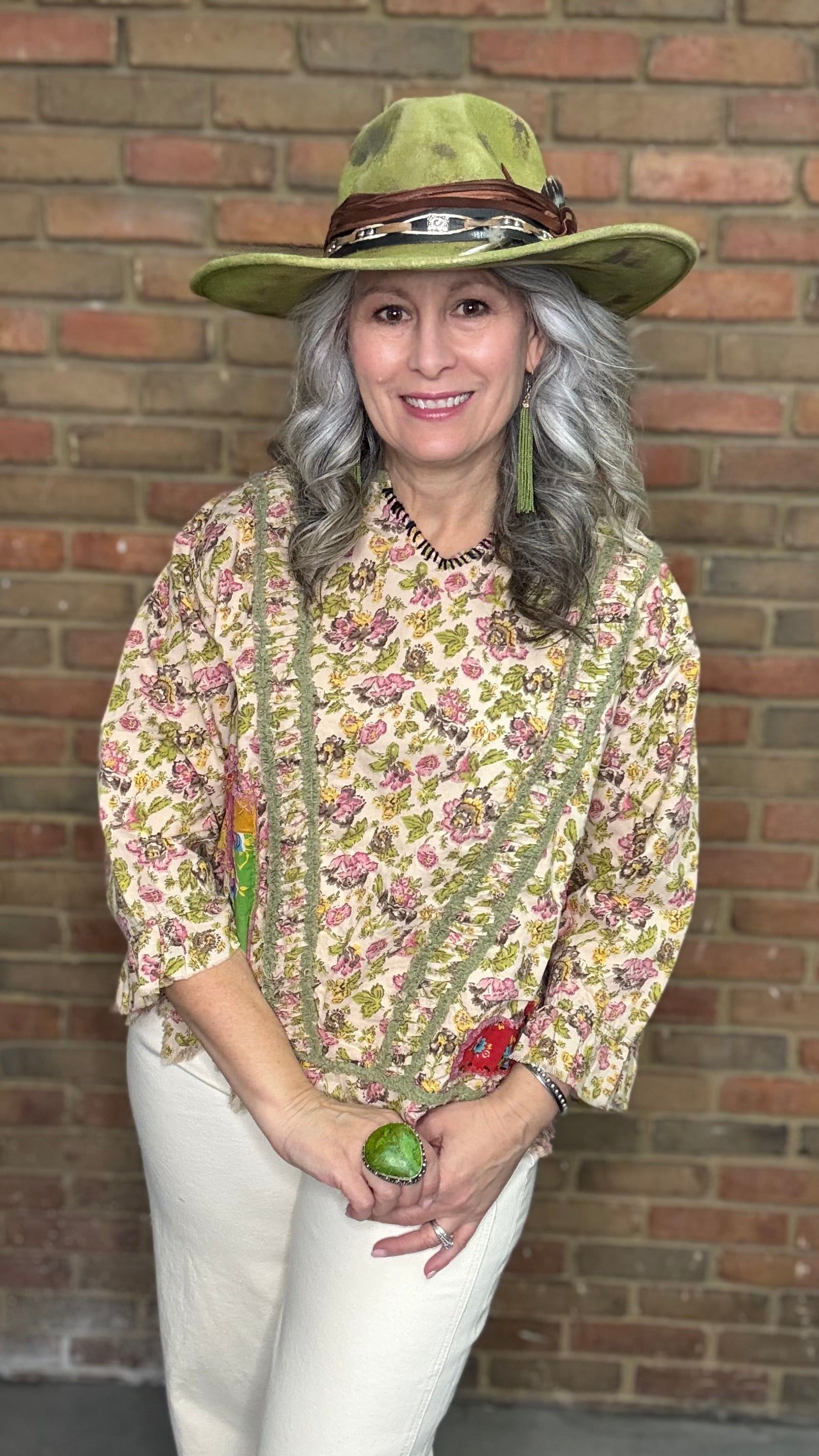Woman wearing Desert Winds Top and wide-brimmed hat against a brick wall.