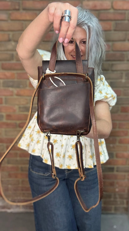 Woman holding a Backpack style leather Handbag with a brick wall in background.