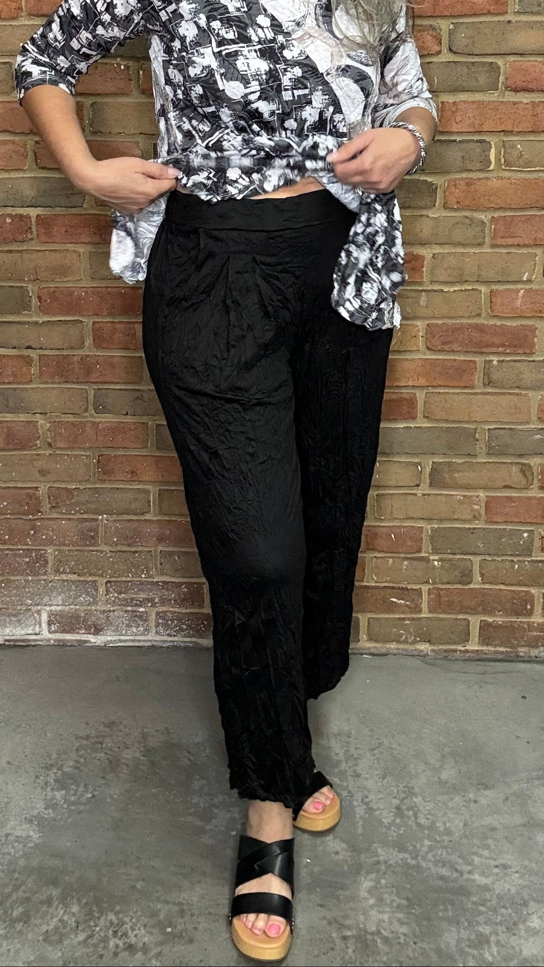 Woman wearing a patterned top and Black Capri Straight Leg Pant standing against a brick wall.