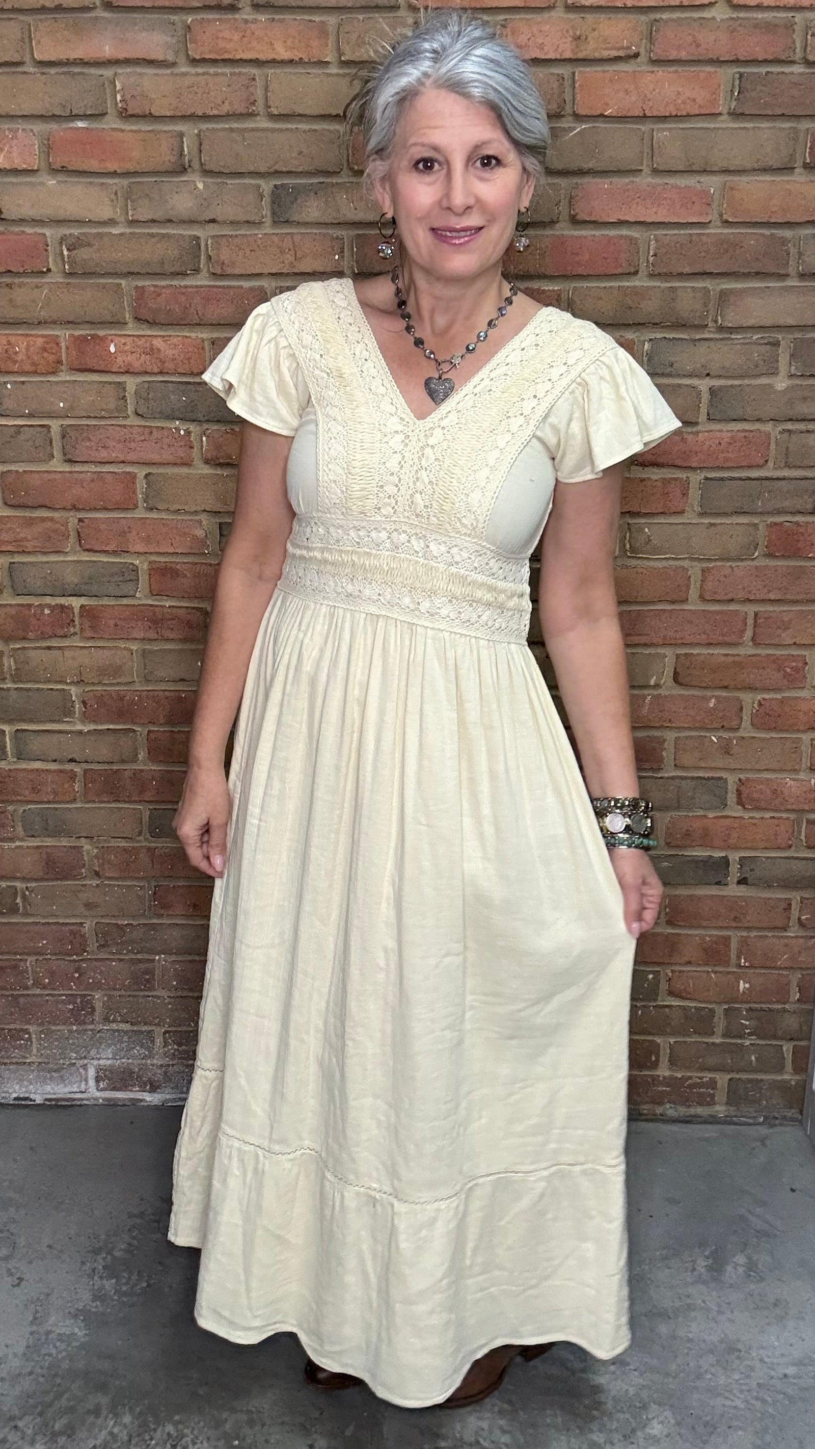 Woman in the Vina Cotton Lace Dress in Ivory standing against a brick wall