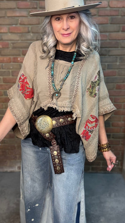 Woman wearing Garden Drift Top with a hat, jeans, and belt against a brick wall.