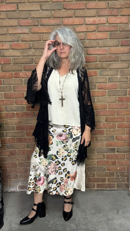 Woman in a floral skirt and black top standing against a brick wall.