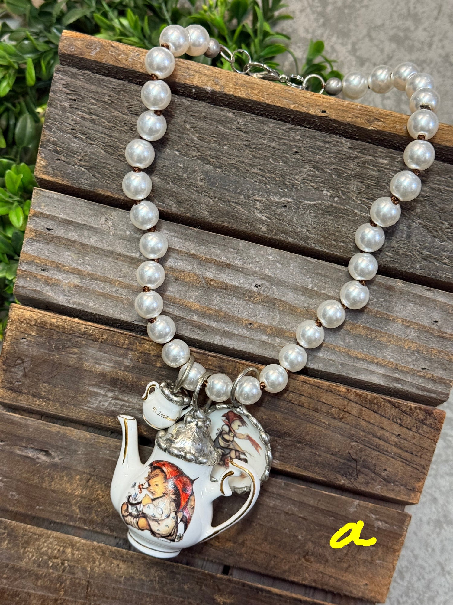 Pearl necklace with a silver teapot charm on a wooden surface