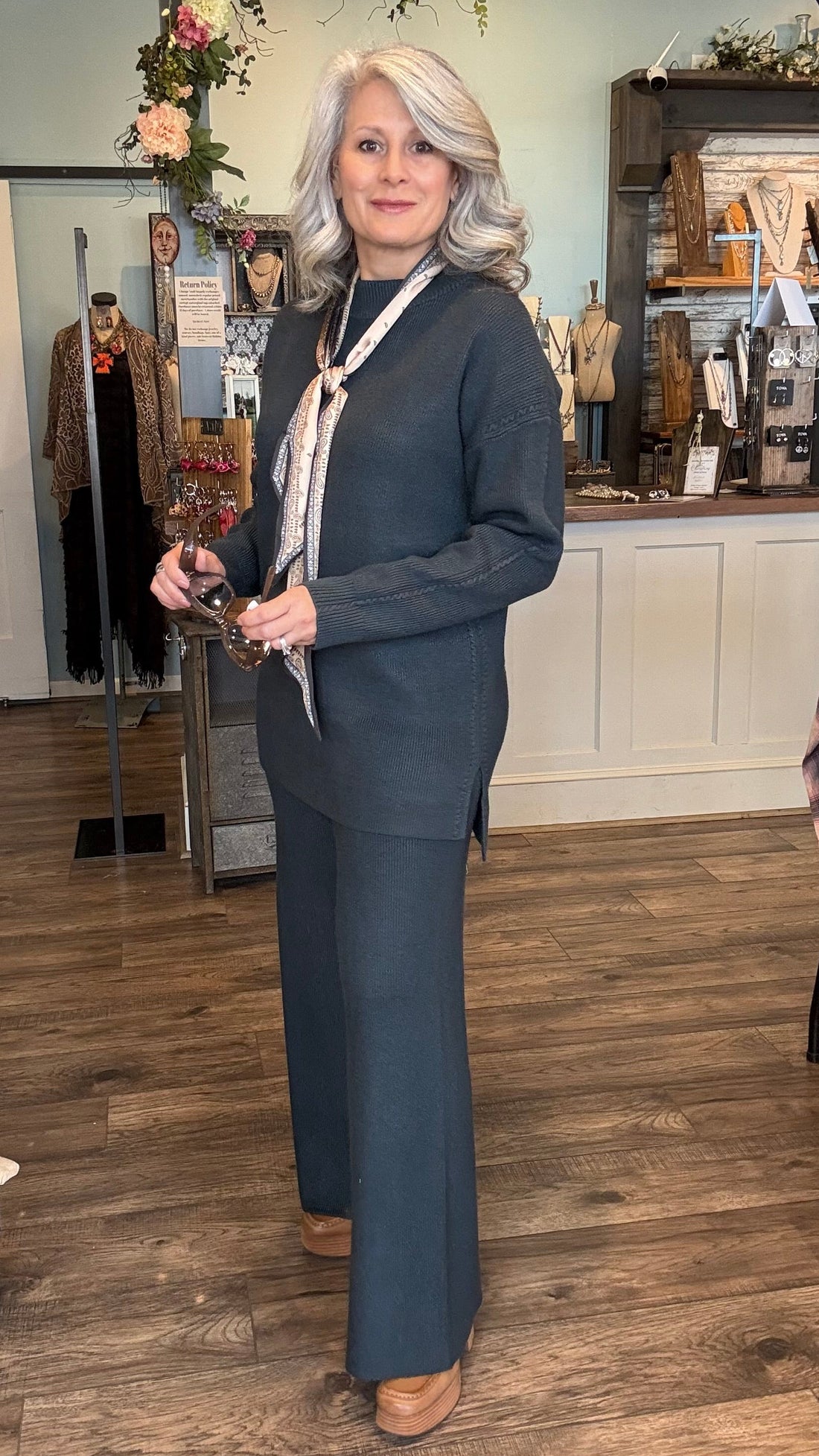 Woman in a denim/teal sweater set standing in a store with clothing racks and displays.