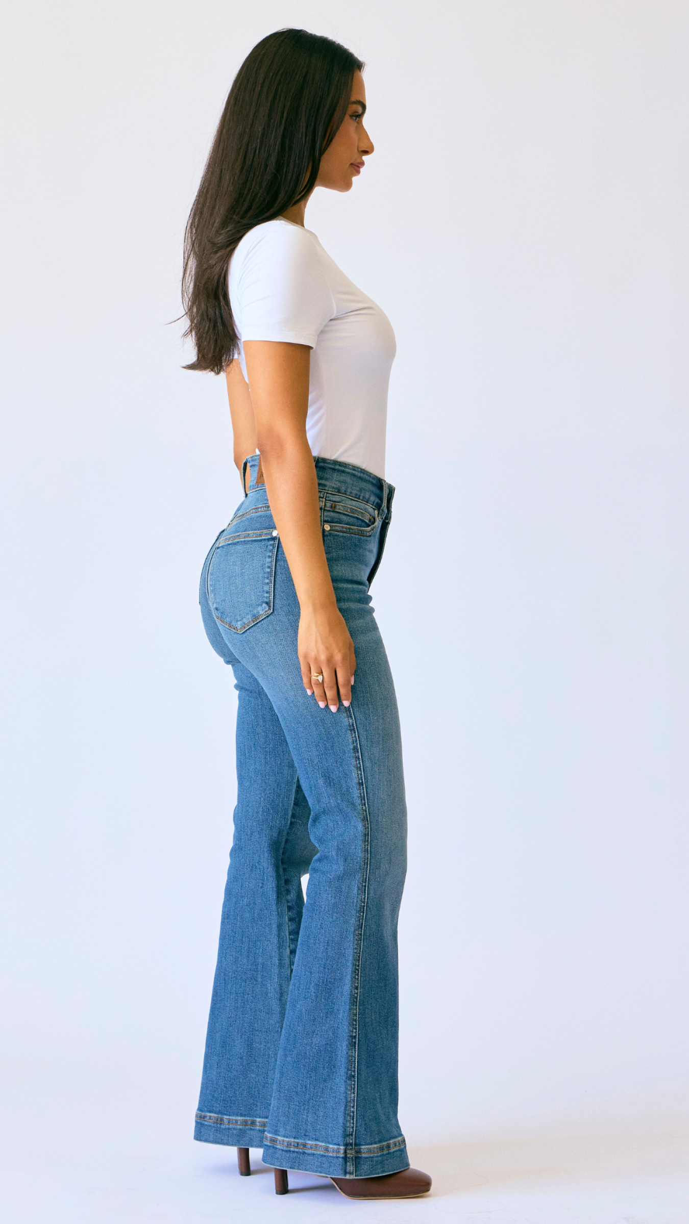 Woman wearing blue flared jeans and a white top on a white background