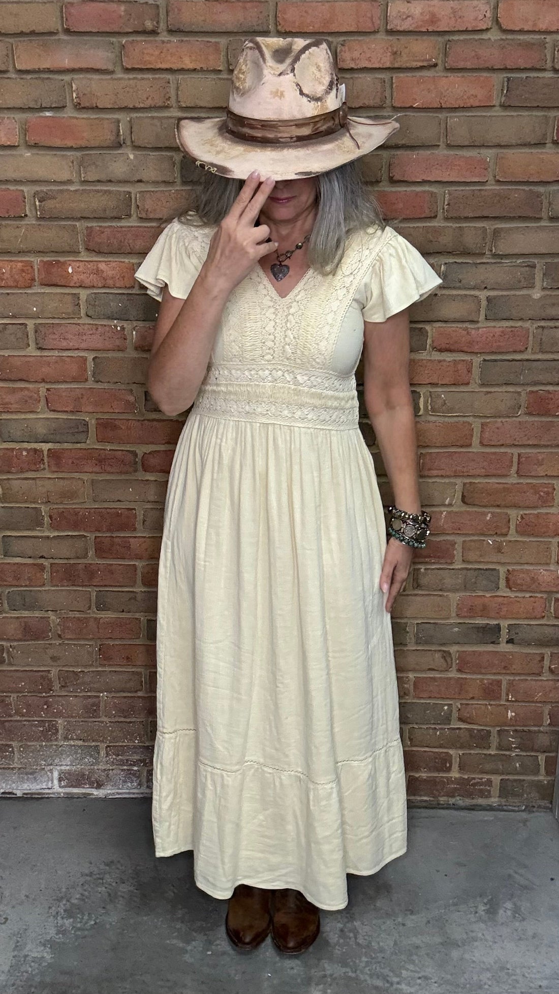 Person wearing the Vina Cotton Lace Dress in Ivory and hat against a brick wall.