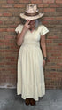 Person wearing the Vina Cotton Lace Dress in Ivory and hat against a brick wall.