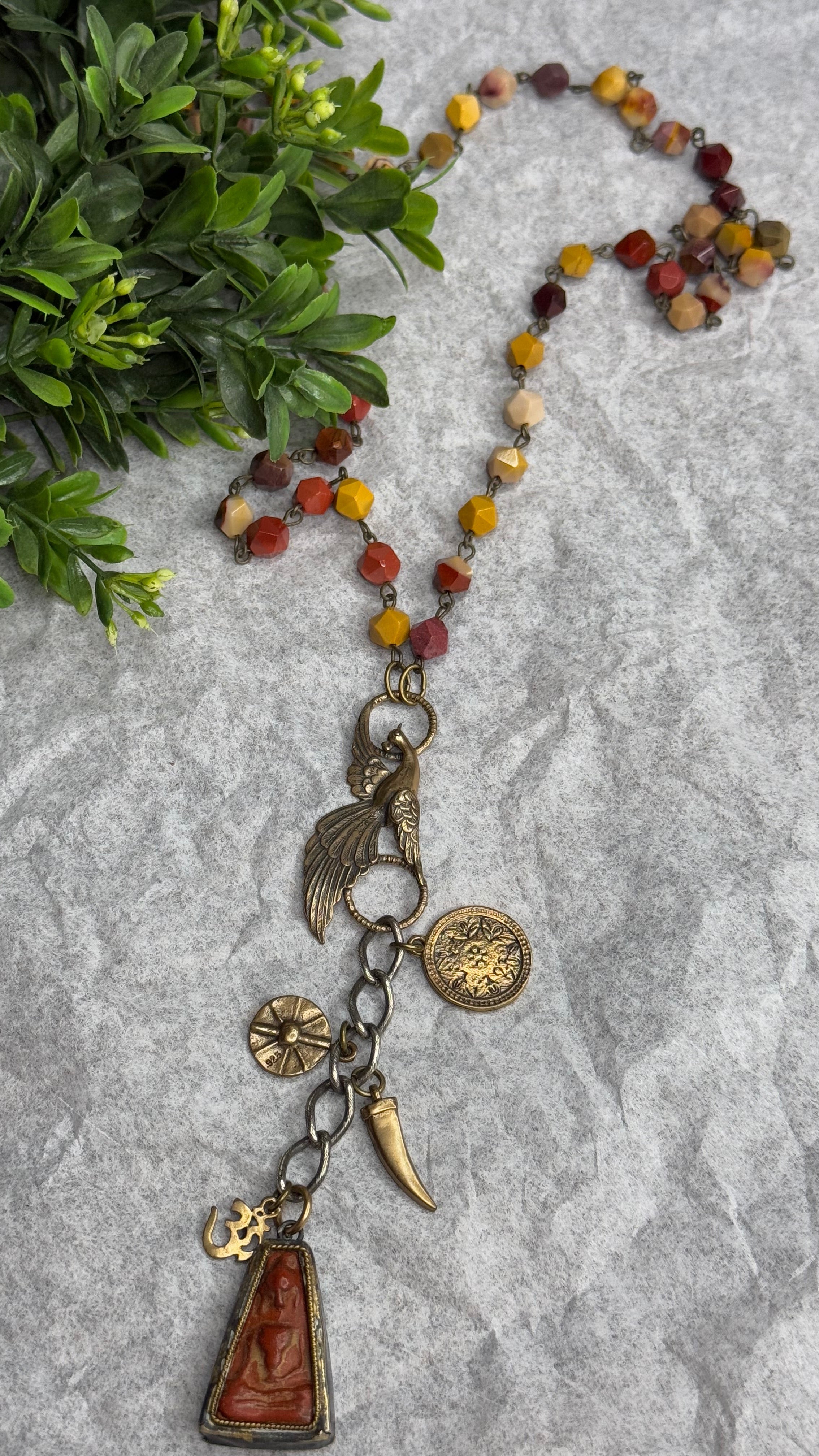 Necklace with various charms on a textured surface with greenery