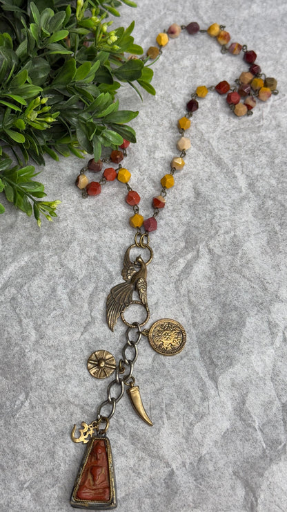 Necklace with various charms on a textured surface with greenery