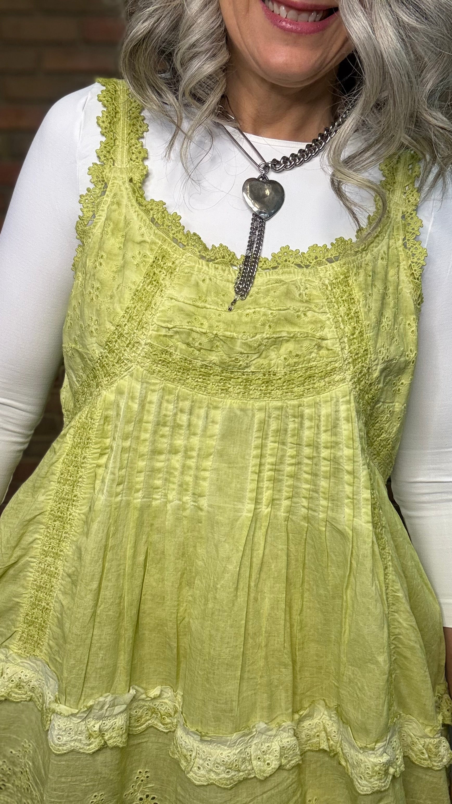 Woman wearing Eyelet Lace Tank over a white shirt, standing against a brick wall.