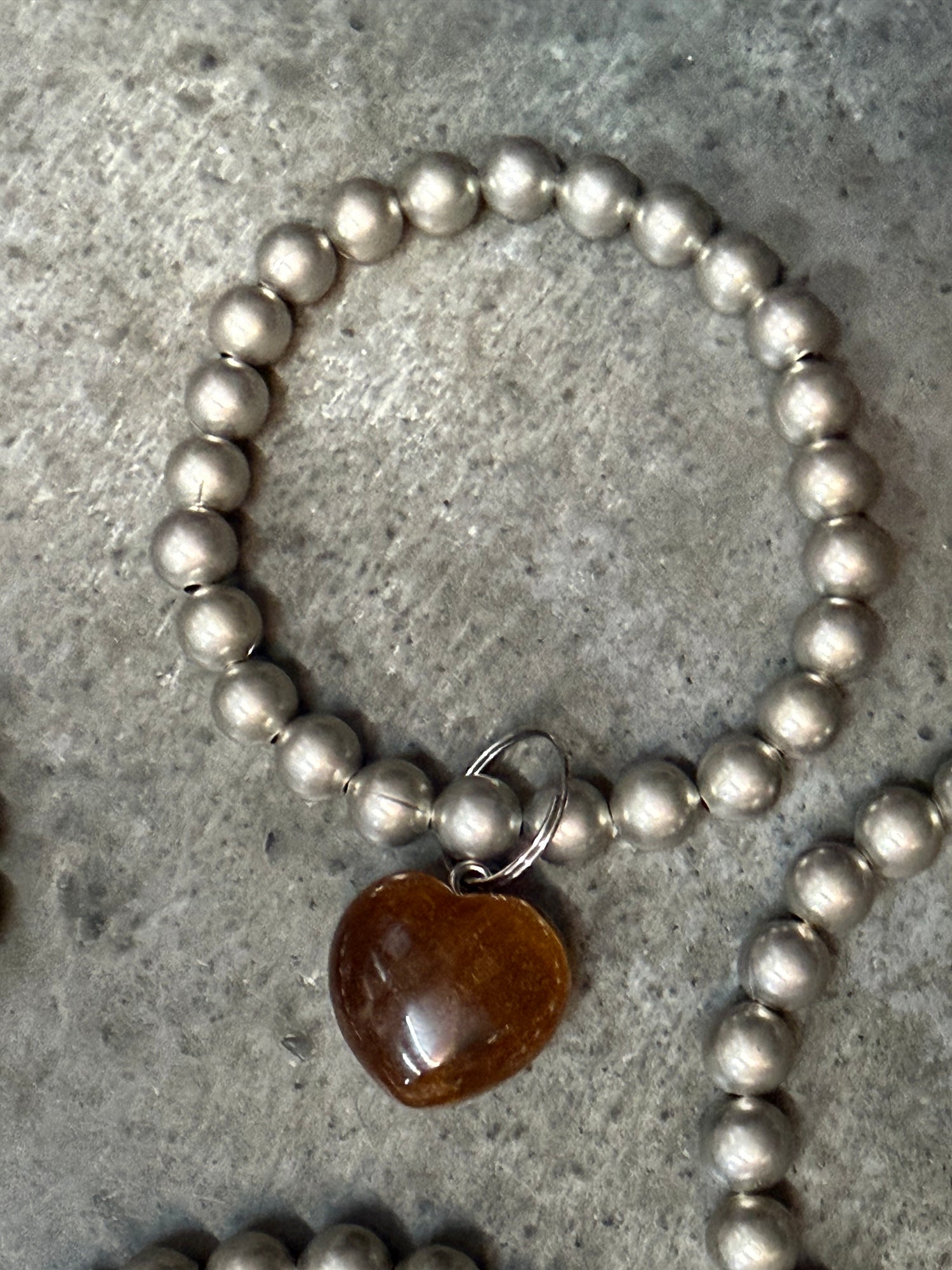 Silver beaded bracelet with a heart-shaped brown stone on a concrete surface