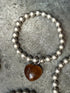 Silver beaded bracelet with a heart-shaped brown stone on a concrete surface
