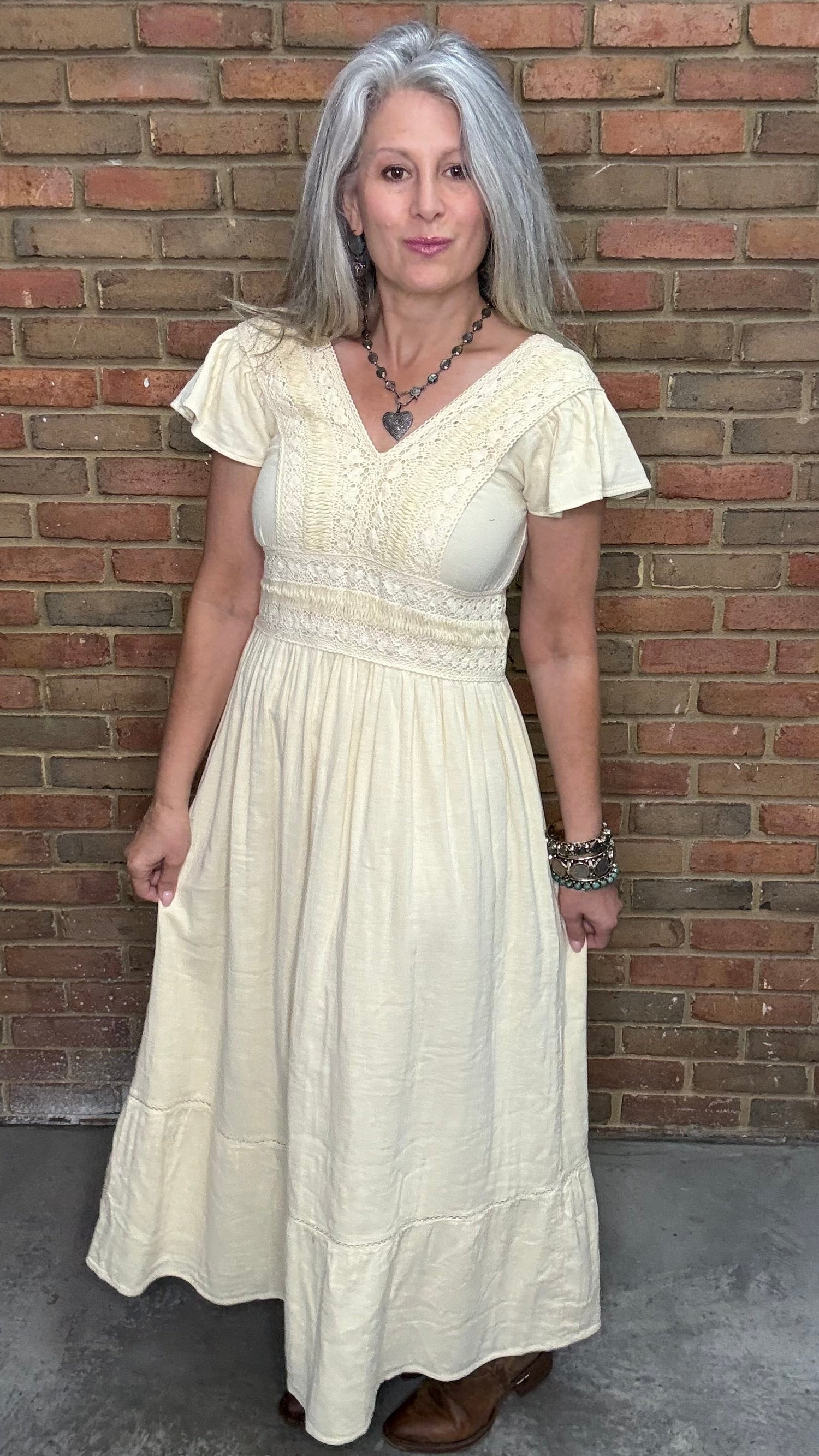 Woman in the Vina Cotton Lace Dress in Ivory standing against a brick wall