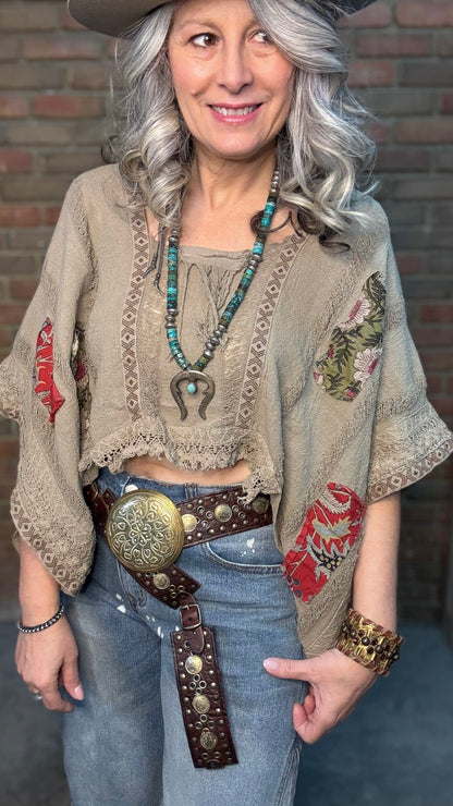 Woman wearing Garden Drift Top with a hat, jeans, and belt against a brick wall.