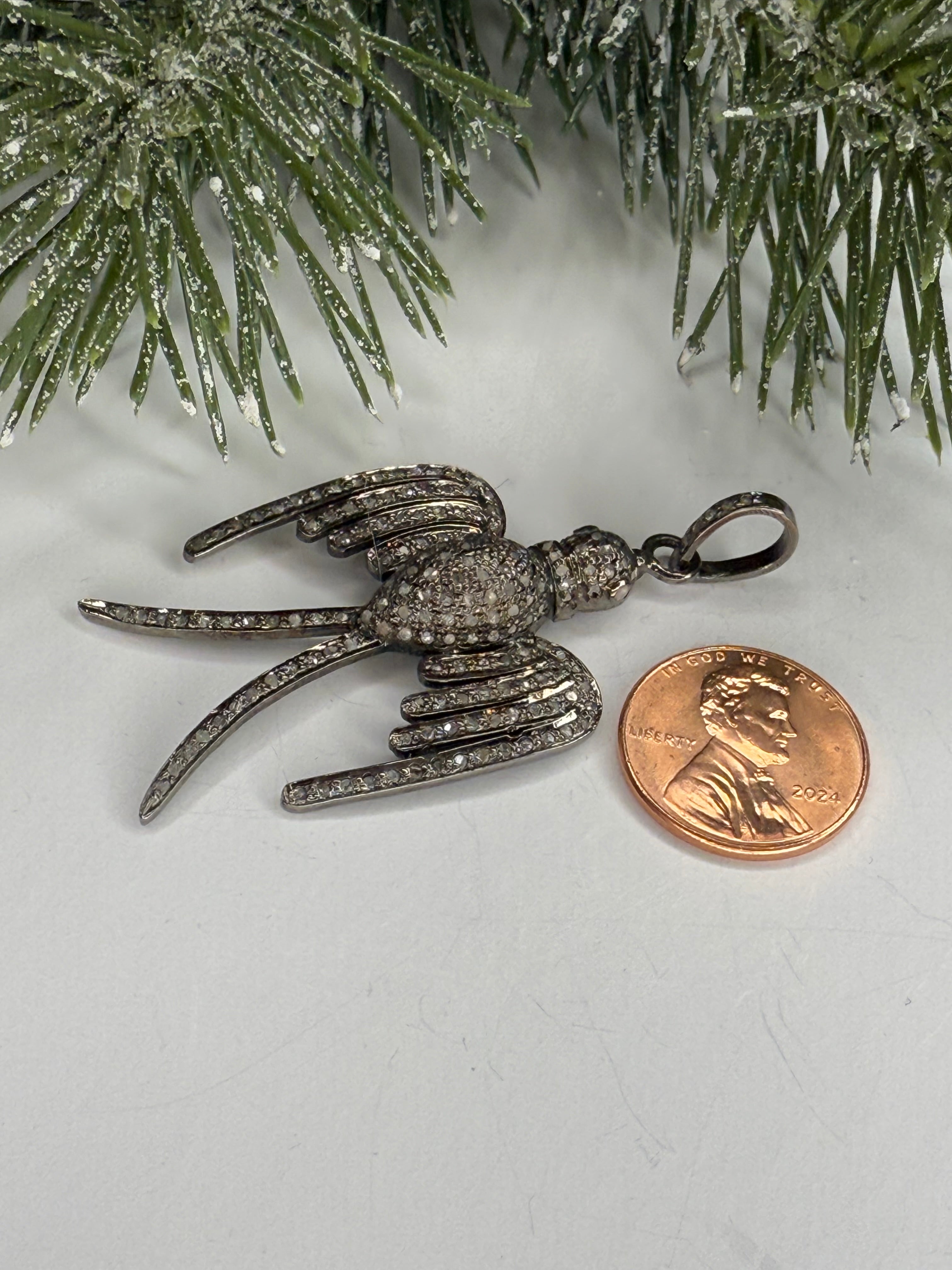 Bird shaped pendant next to a penny on a white surface with greenery.