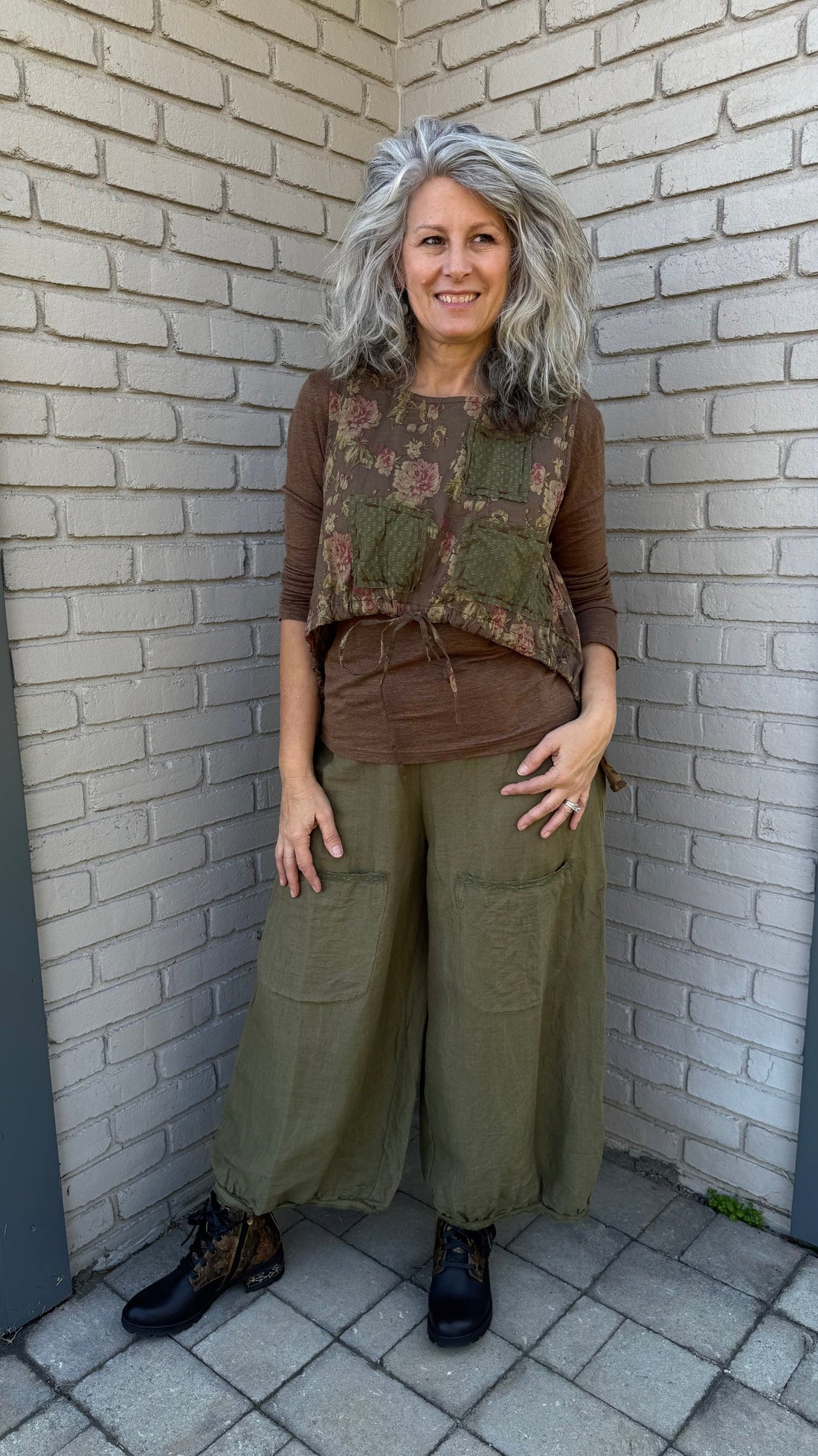 Person wearing a floral vest and green pants standing on a tiled floor.