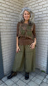 Person wearing a floral vest and green pants standing on a tiled floor.