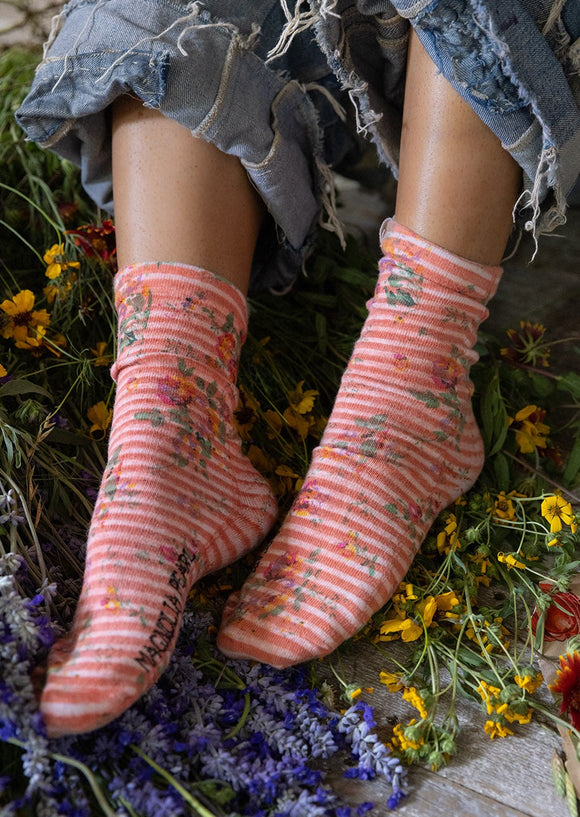 Blockprint Magnolia Pearl Socks in the color Loonette on feet on a bed of flowers.