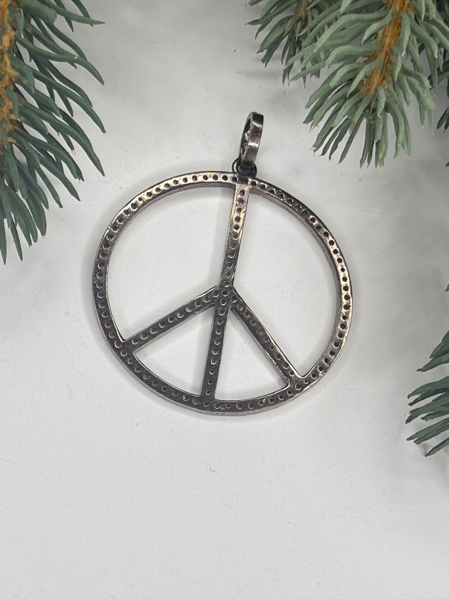 Back of silver peace sign pendant on a white background with greenery