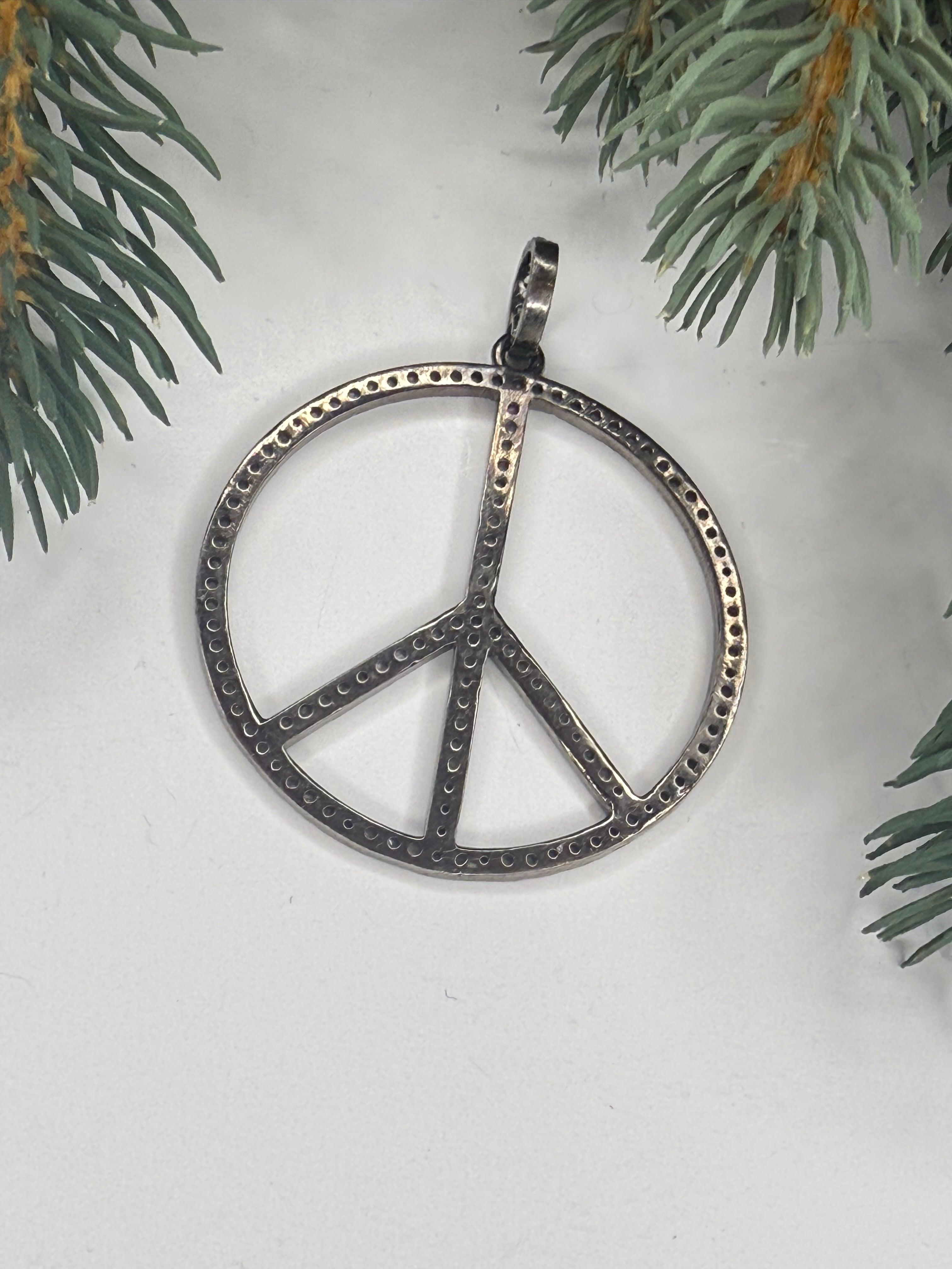 Back of silver peace sign pendant on a white background with greenery