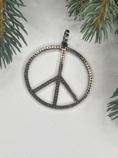 Back of silver peace sign pendant on a white background with greenery