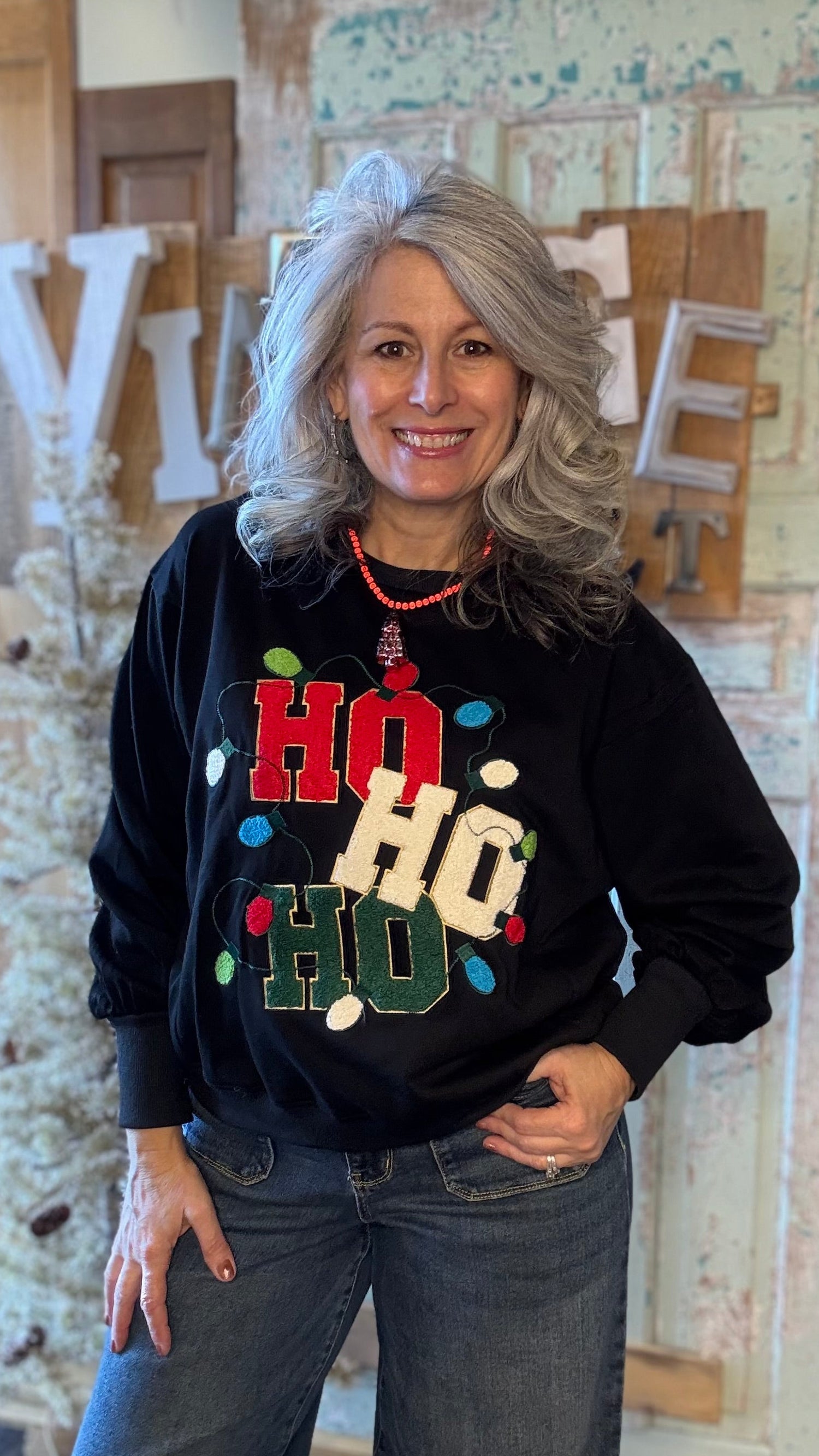 Woman wearing a black sweater with colorful text and lights, standing in a rustic indoor setting.