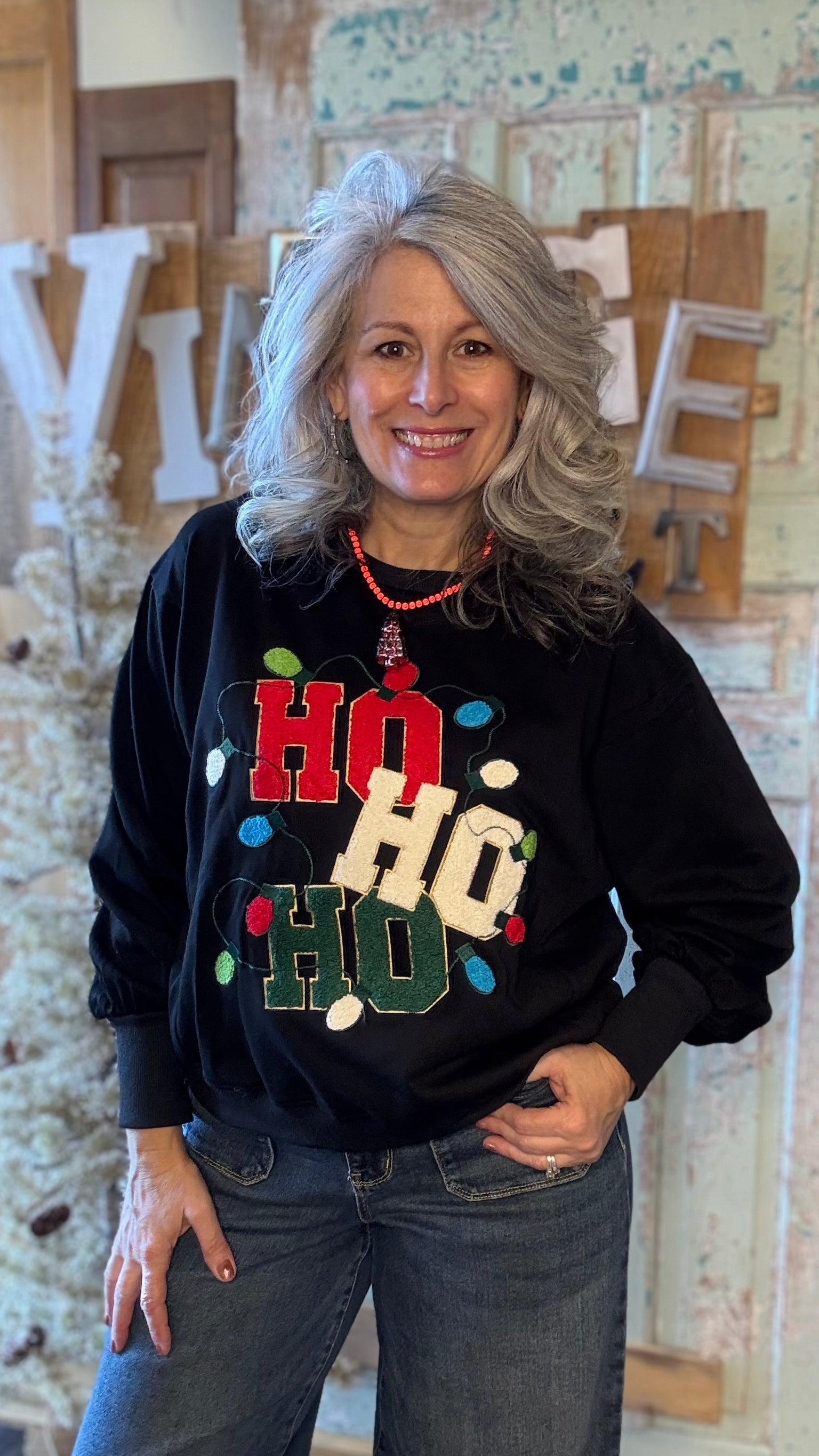 Woman wearing a black sweater with colorful text and lights, standing in a rustic indoor setting.