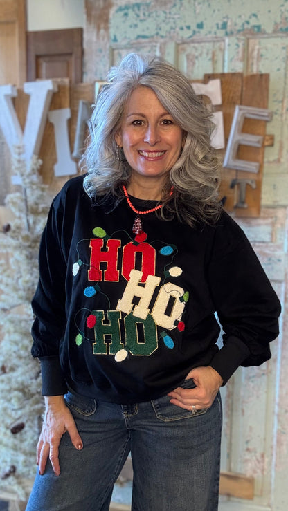 Woman wearing a black sweater with colorful text and lights, standing in a rustic indoor setting.