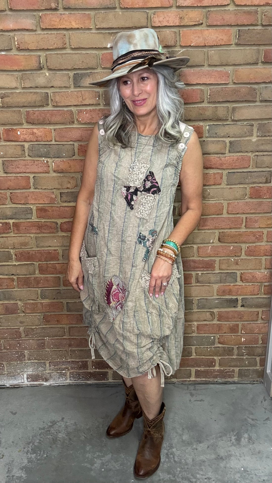 Woman wearing a patterned dress with butterfly designs against a brick wall.