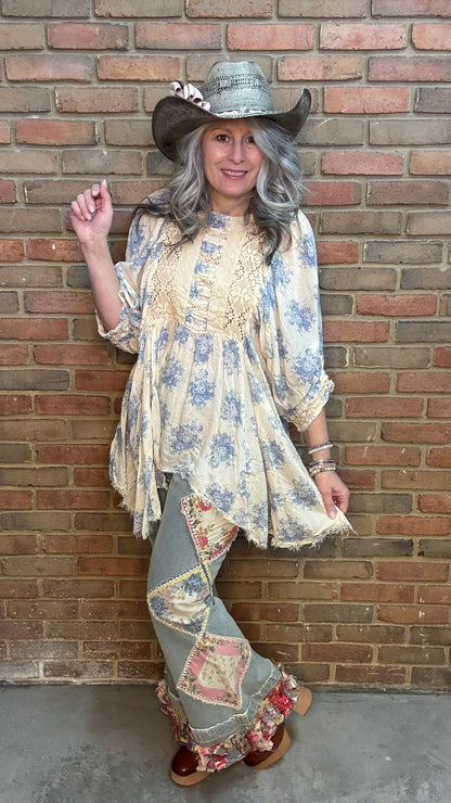 Woman in a Whispering Blue Bell Dress and flared pants standing against a brick wall.
