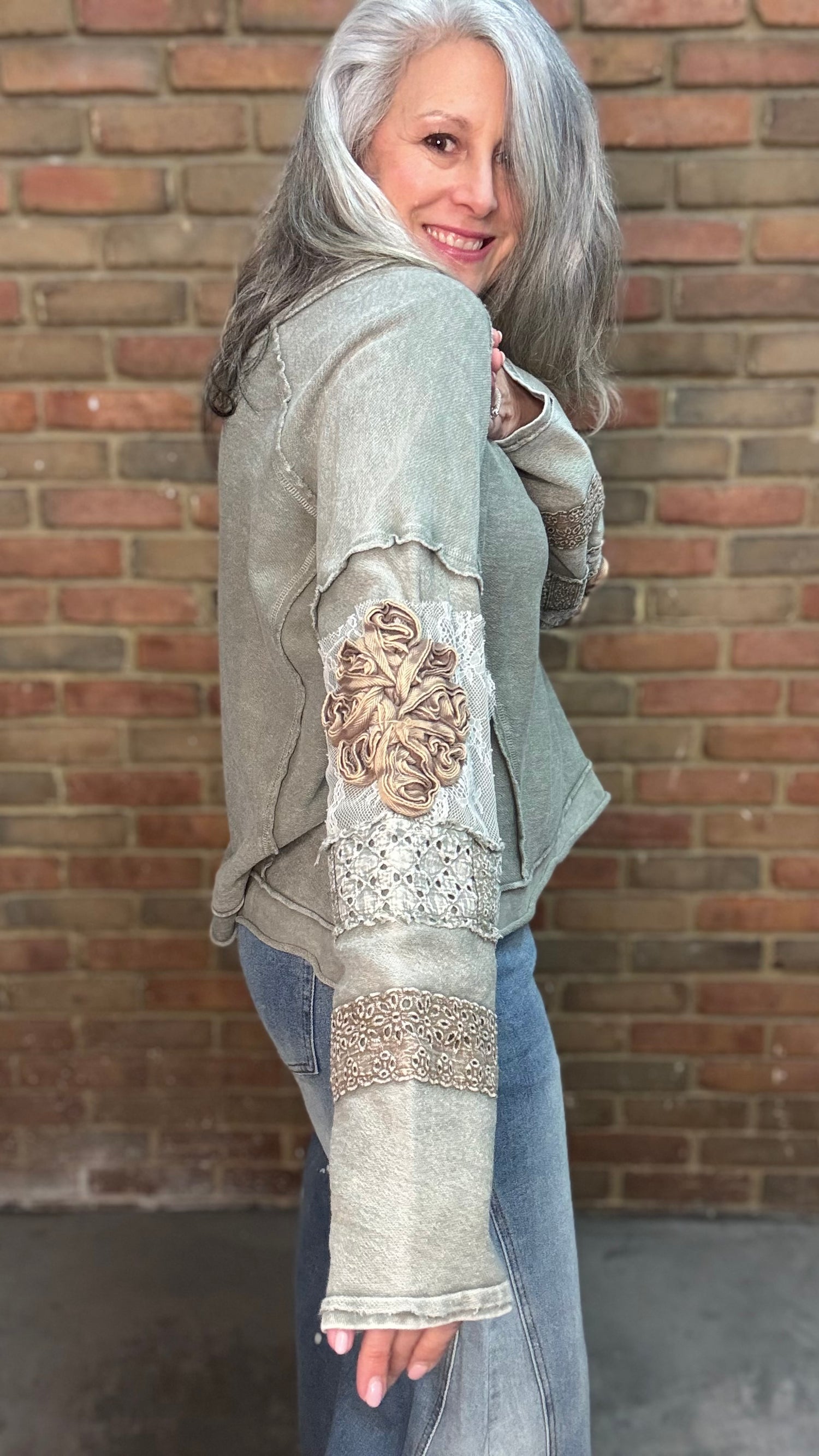 Woman wearing the Olive Embellished Sleeve Top and Bleached Wide Leg Jeans standing against a brick wall.
