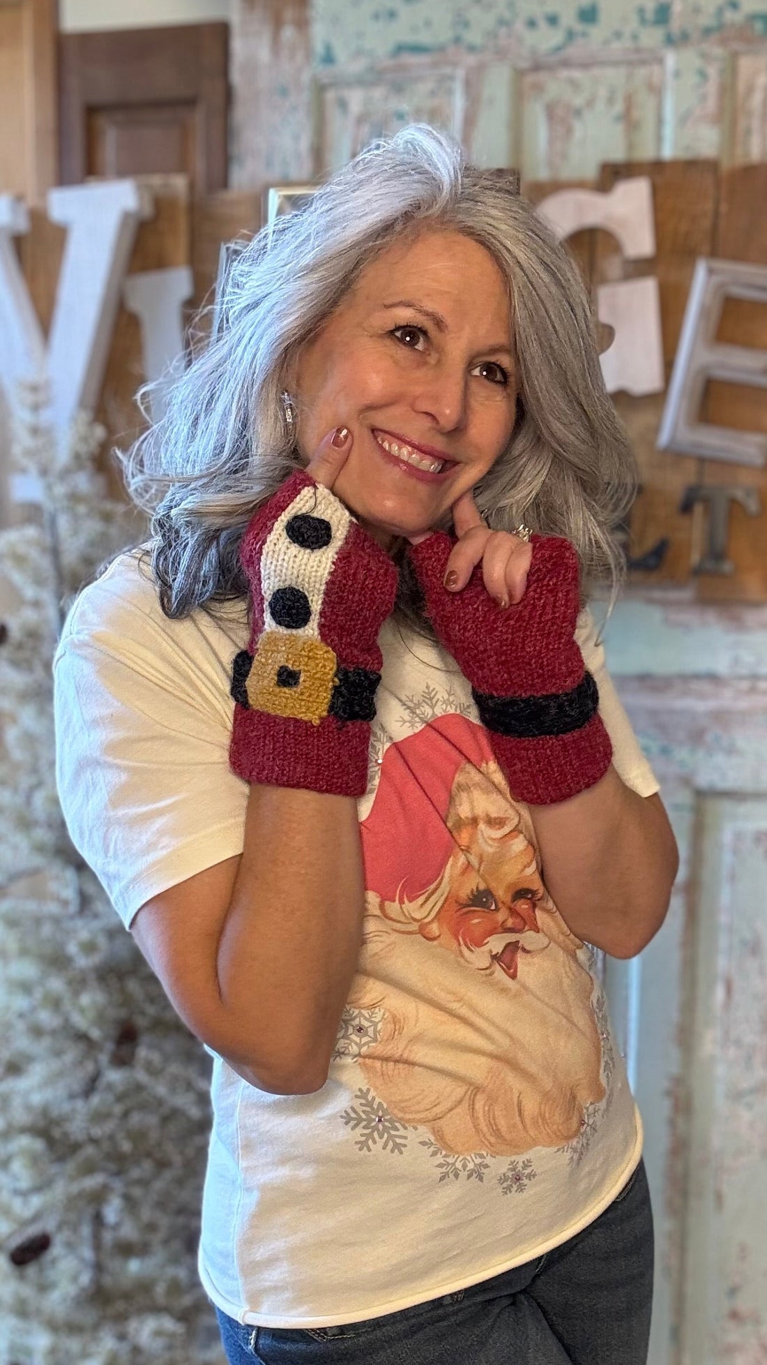Woman wearing a white shirt with a graphic design, dark pants, and red fingerless gloves in a rustic indoor setting.
