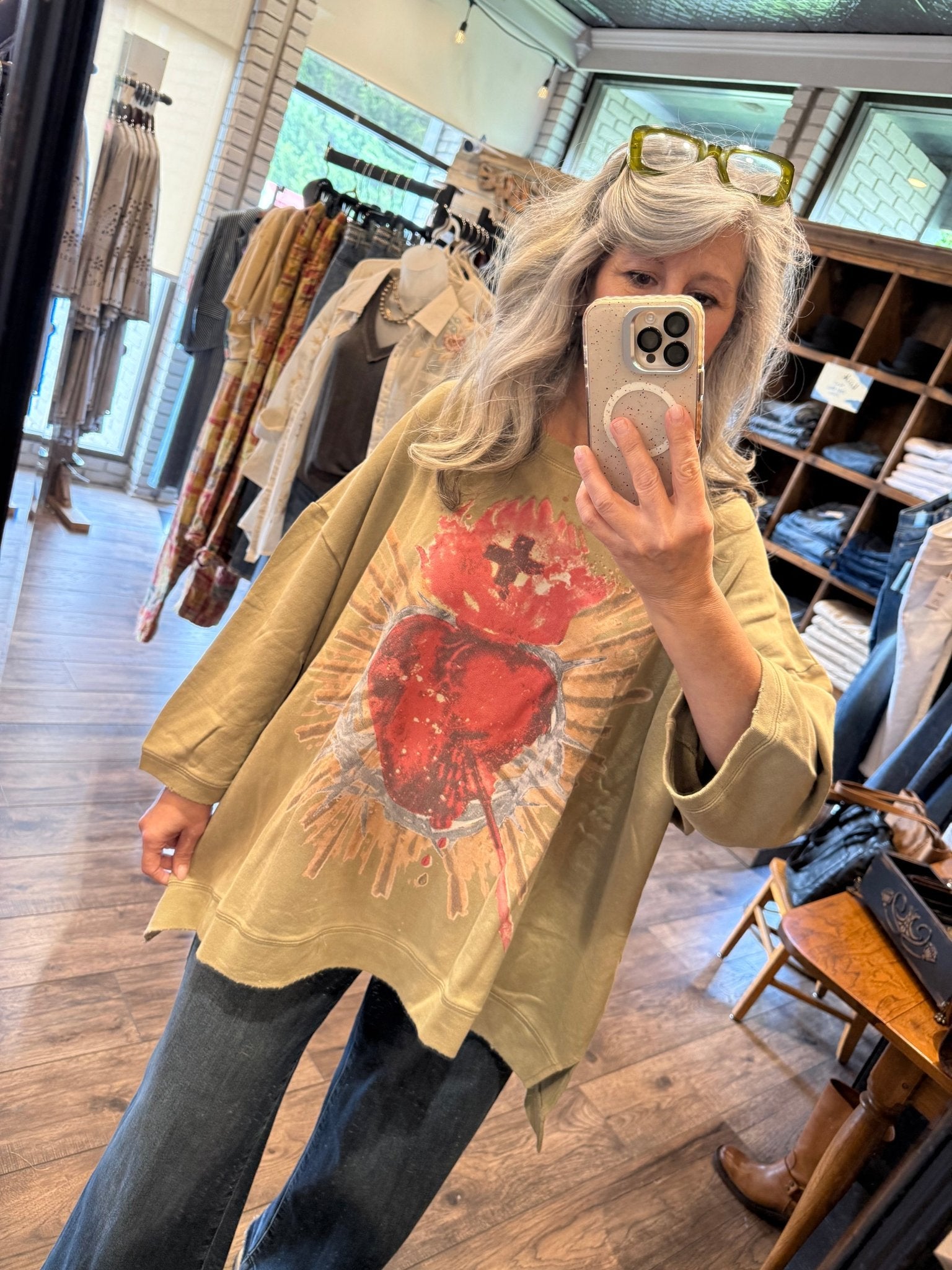 Person wearing a Dance With the Moon Sweatshirt - Olive Sacred with a red graphic design, taking a mirror selfie.