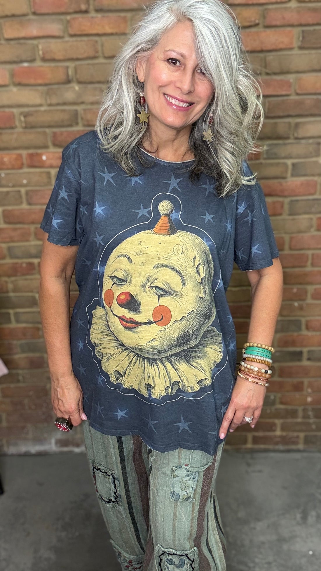 Woman wearing a Moon Dance Tee - Moon Wander with a clown graphic design in front of a brick wall.
