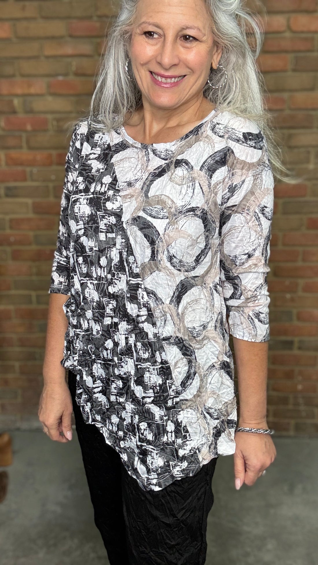 Woman wearing Circles Asymmetric Pocket Top standing in front of a brick wall.