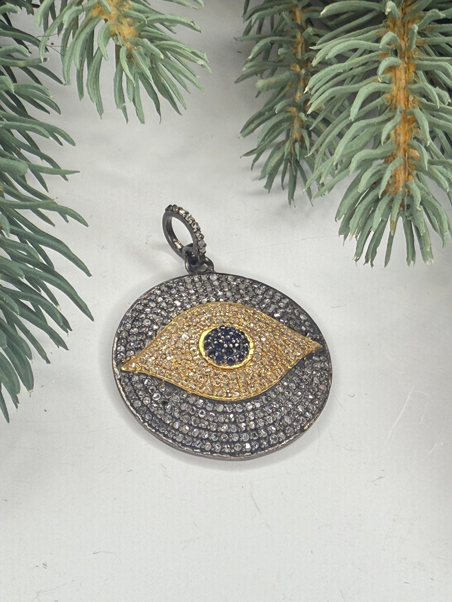 Pave diamond pendant with eye design on a white background with greenery