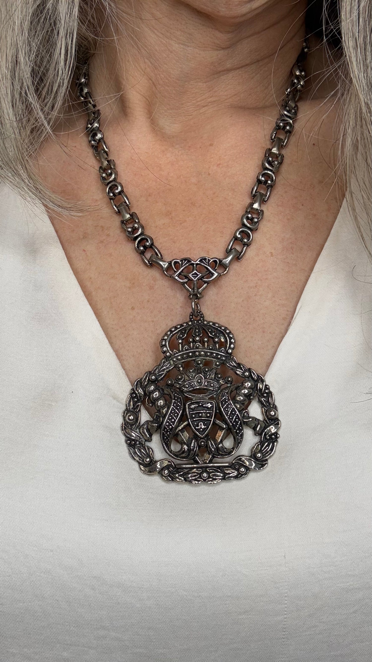 Close-up of a person wearing a detailed necklace with a large pendant on a plain background
