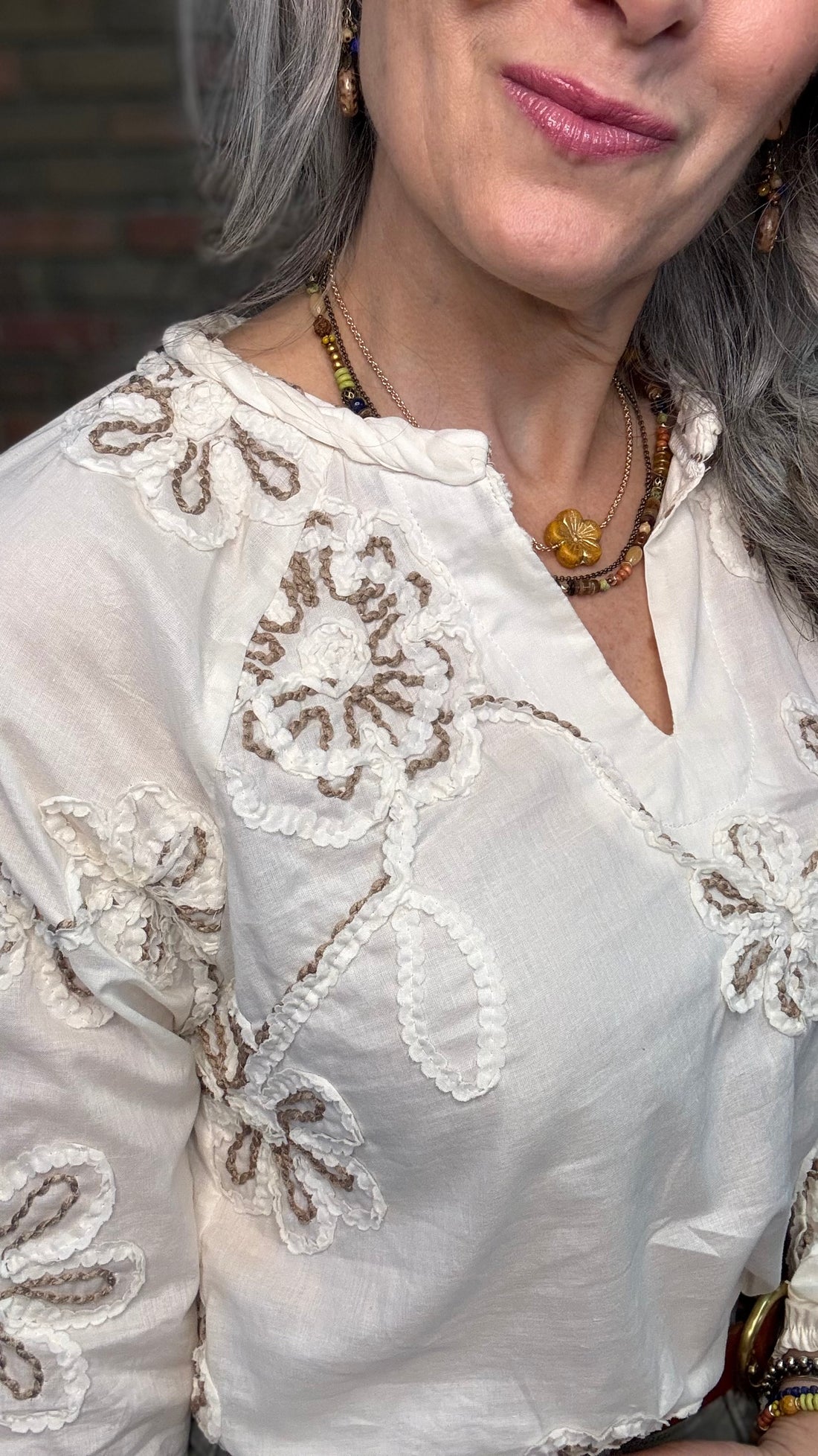 Woman wearing Embroidered Raglan Long Sleeve with Sage pants against brick wall.