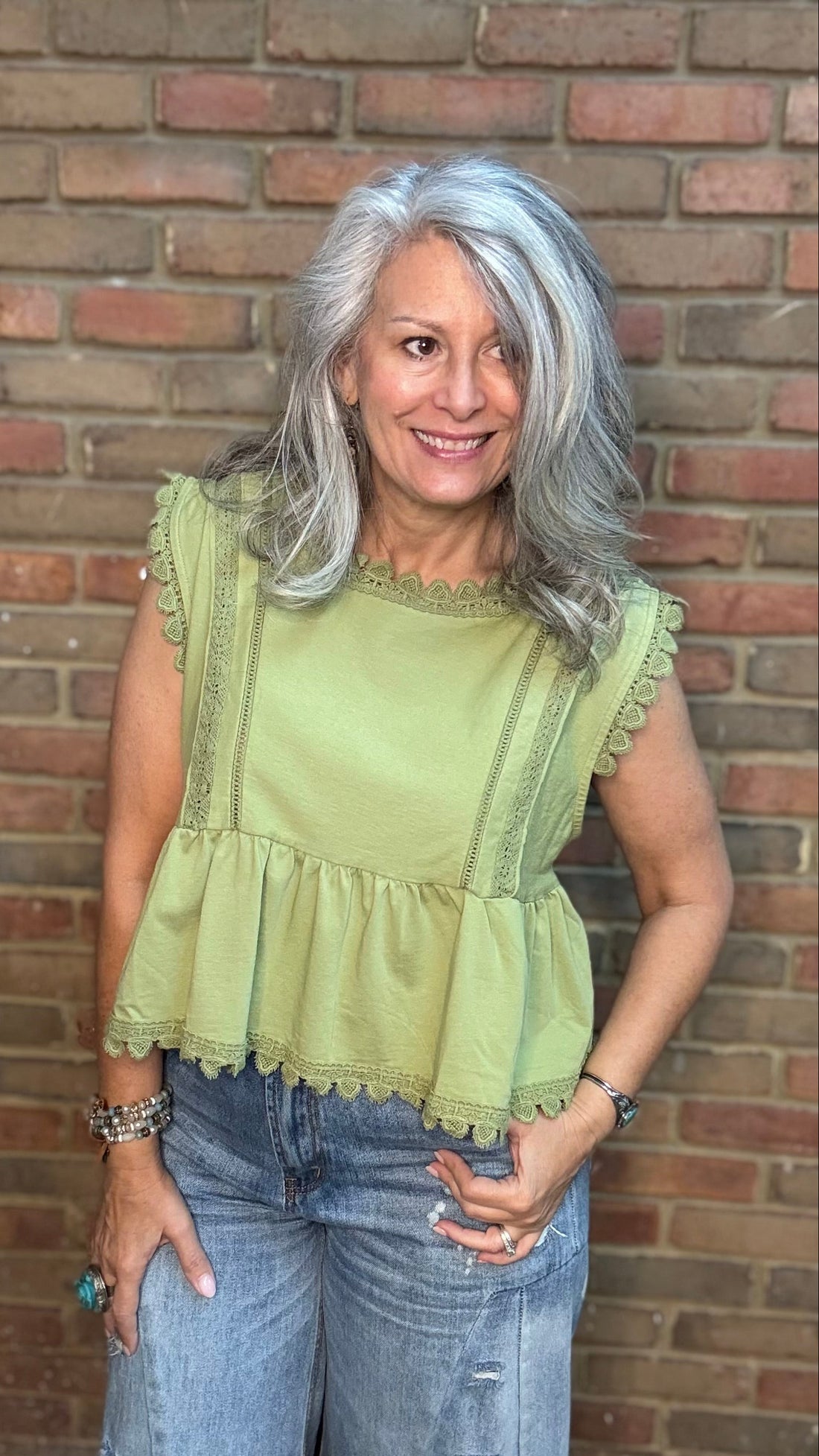 Woman wearing a light green top and blue jeans standing against a brick wall.