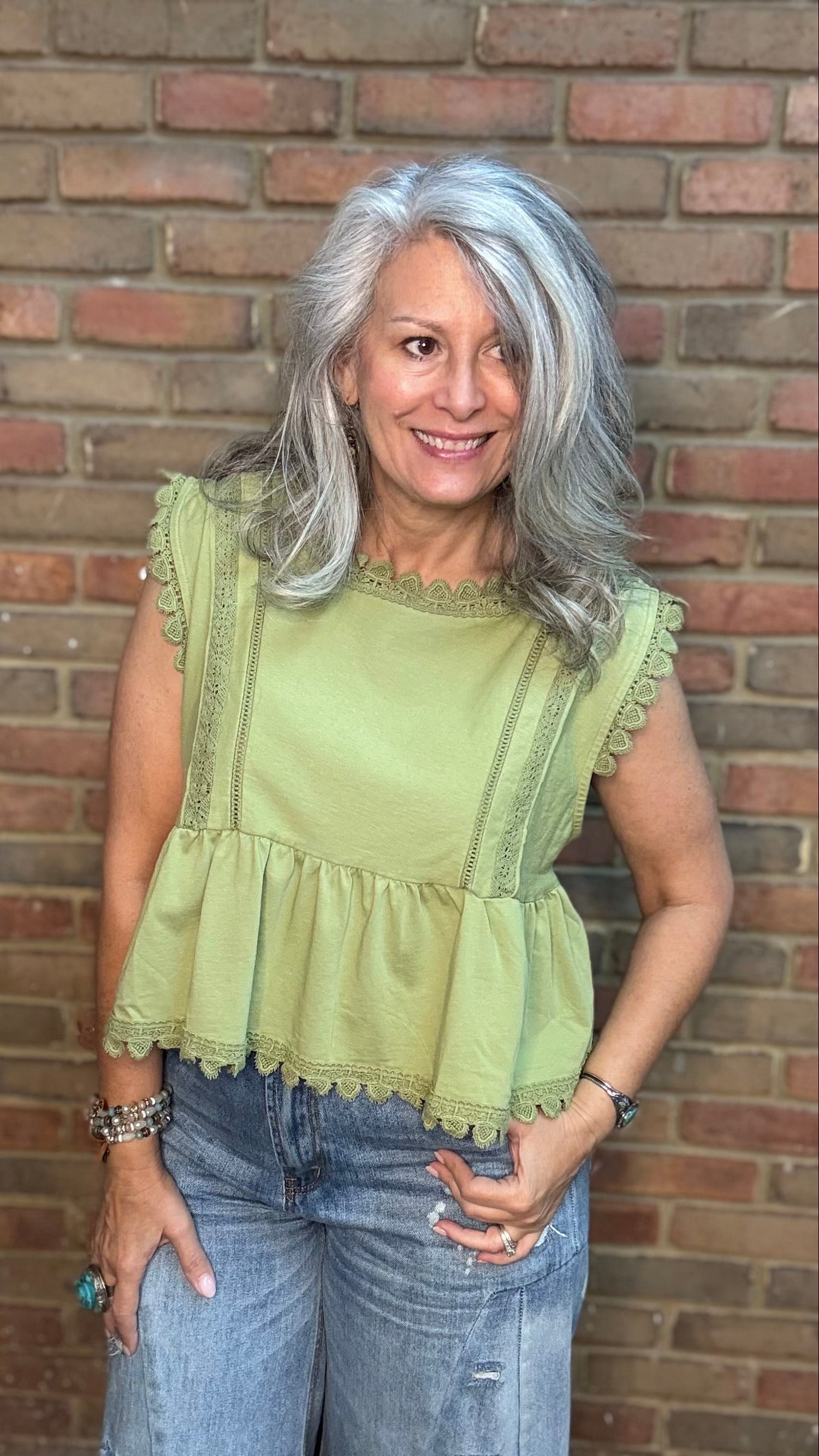Woman wearing a light green top and blue jeans standing against a brick wall.