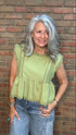Woman wearing a light green top and blue jeans standing against a brick wall.