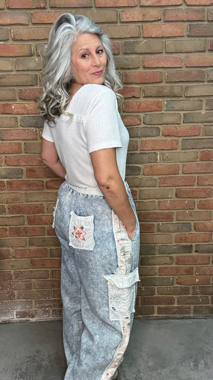 Woman wearing a white top and the Embroidery Patch Denim Joggers, floral embroidery pants leaning against a brick wall.