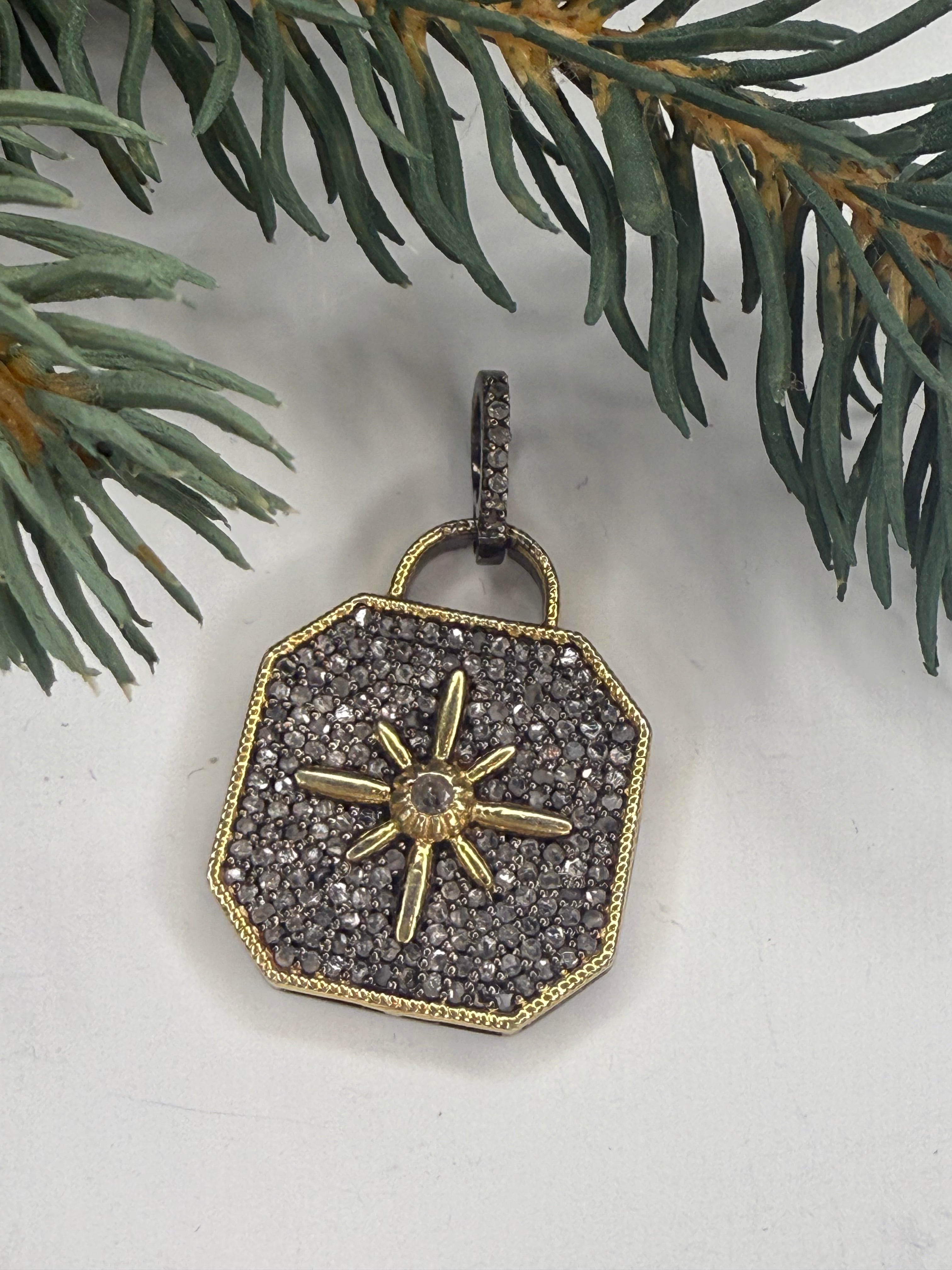 Lock shaped pendant with pave diamonds and a embossed star design on a light background with greenery