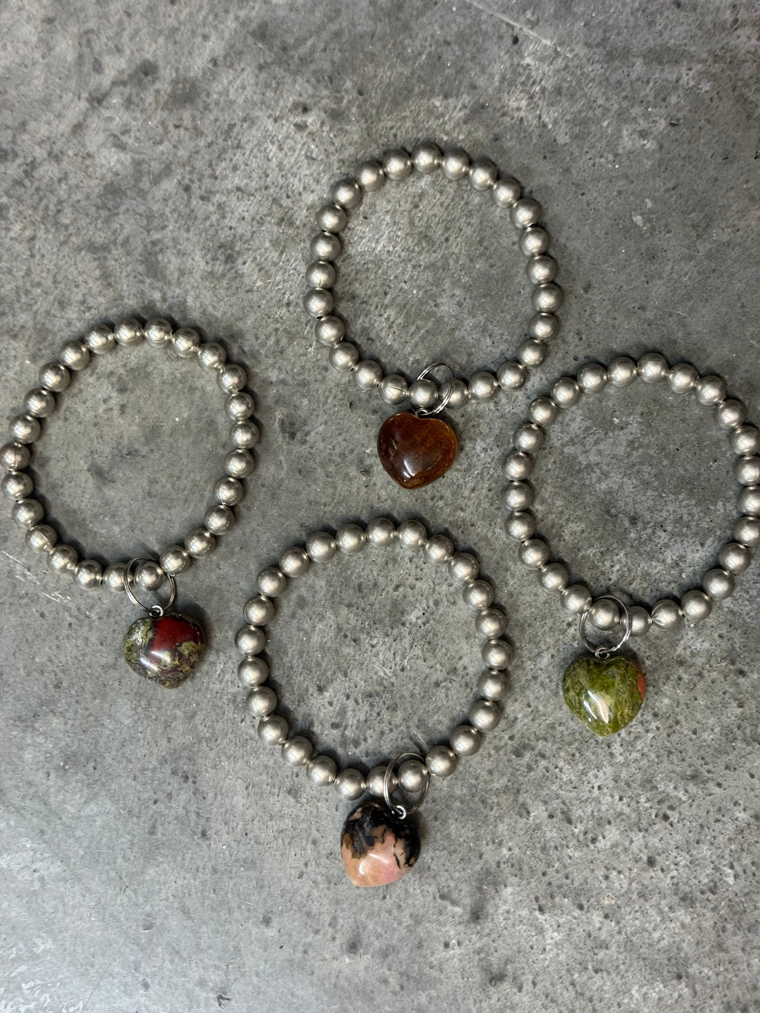 Set of silver beaded bracelets with gemstone beads on a concrete surface