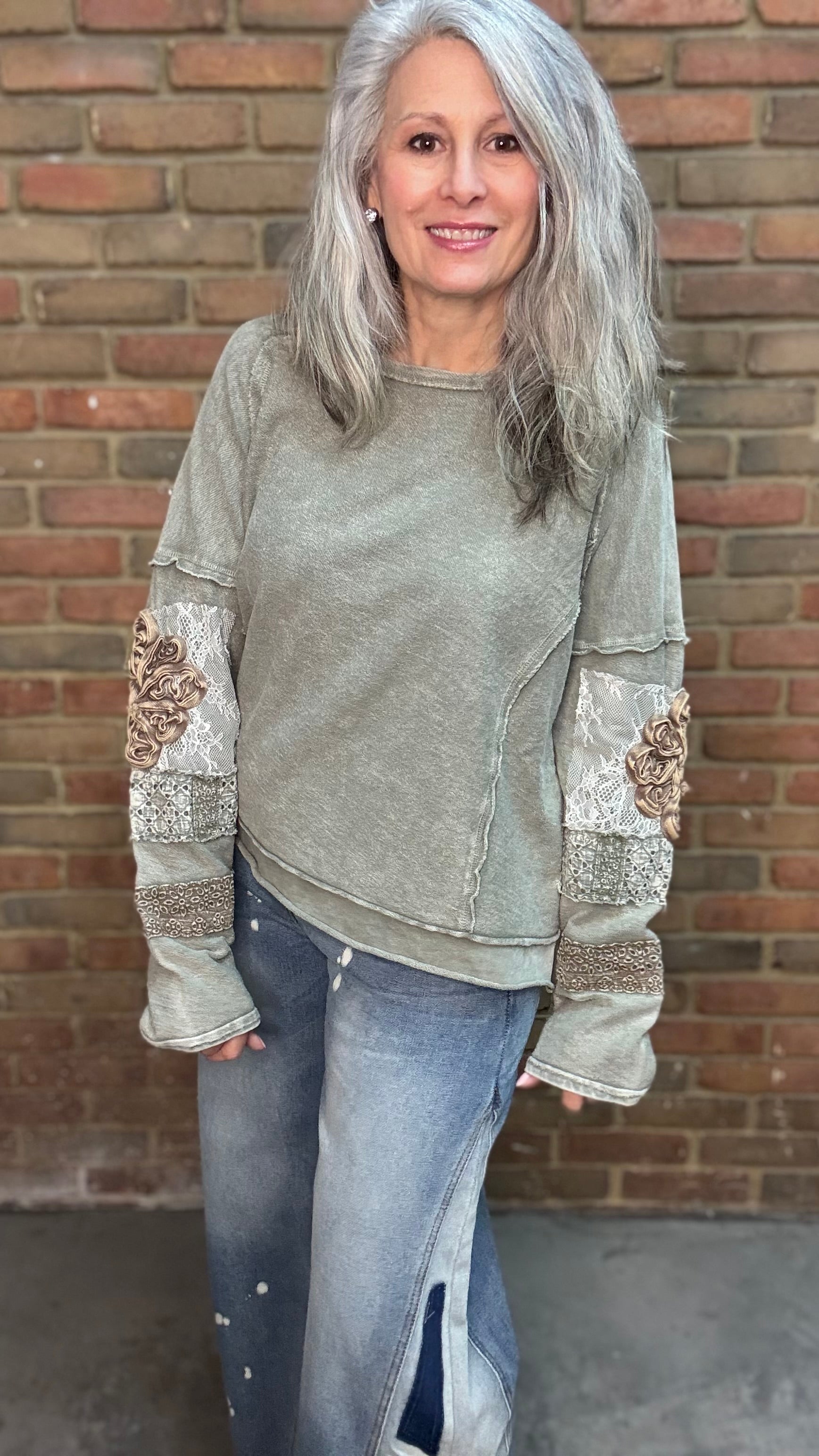 Woman wearing the Olive Embellished Sleeve Top and Bleached Wide Leg Jeans standing against a brick wall.