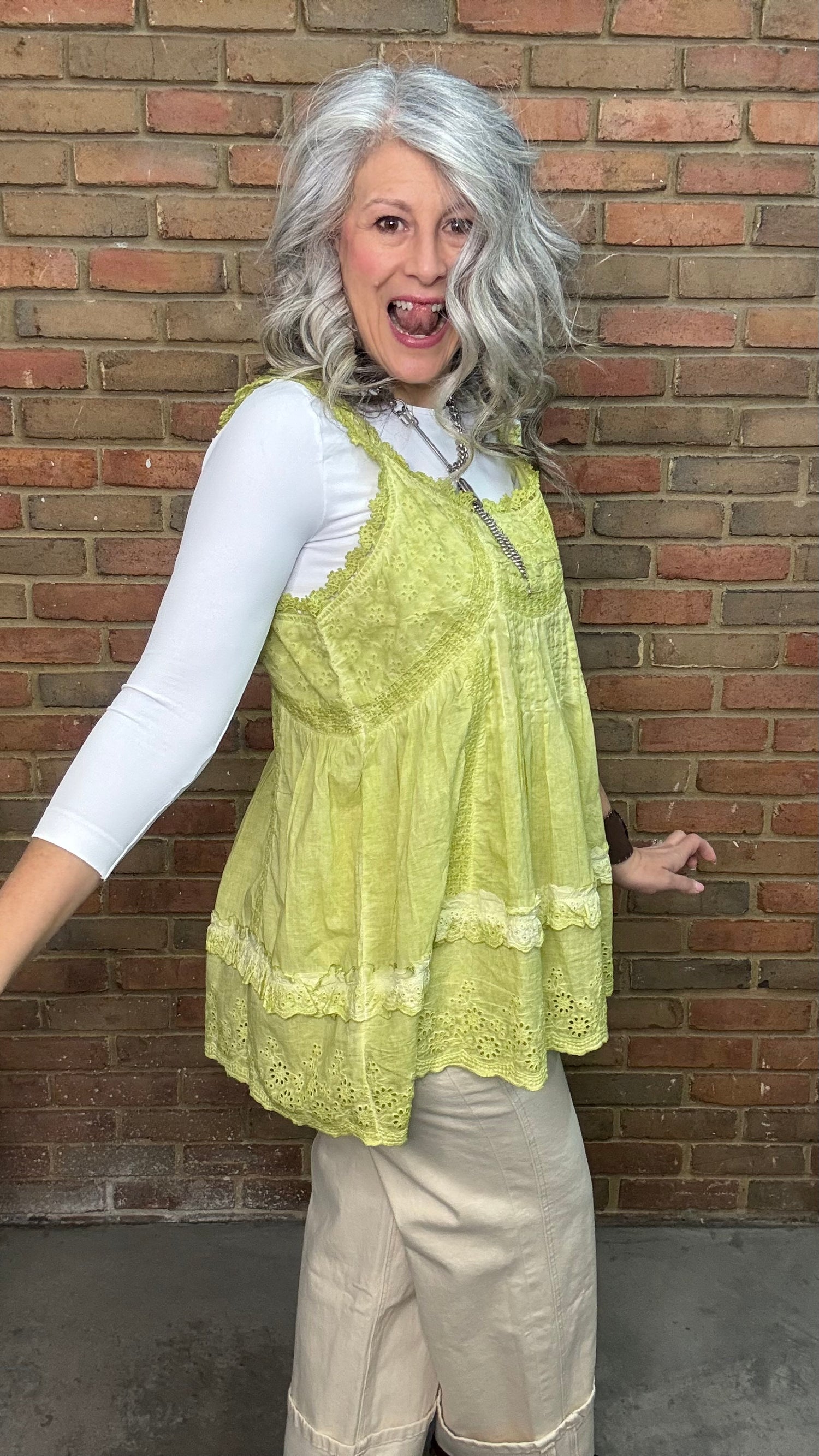 Woman wearing Eyelet Lace Tank over a white shirt, standing against a brick wall.