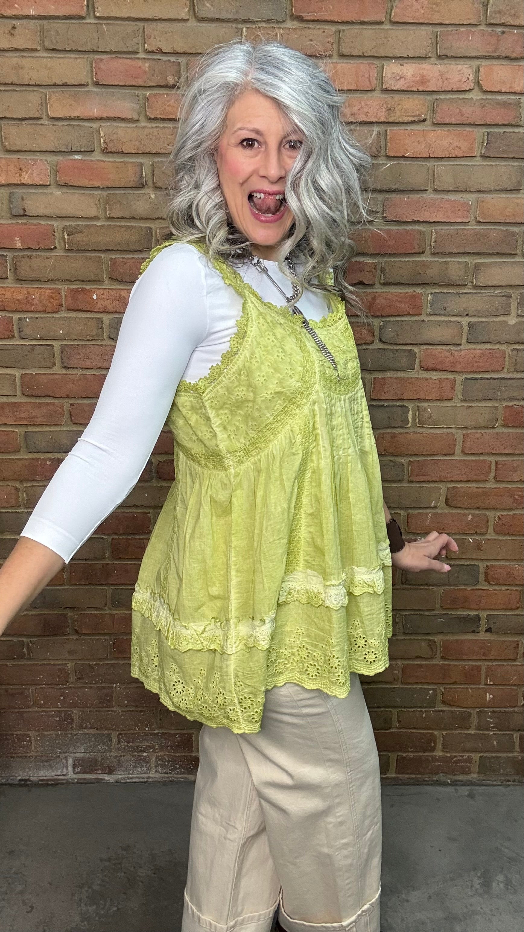 Woman wearing Eyelet Lace Tank over a white shirt, standing against a brick wall.