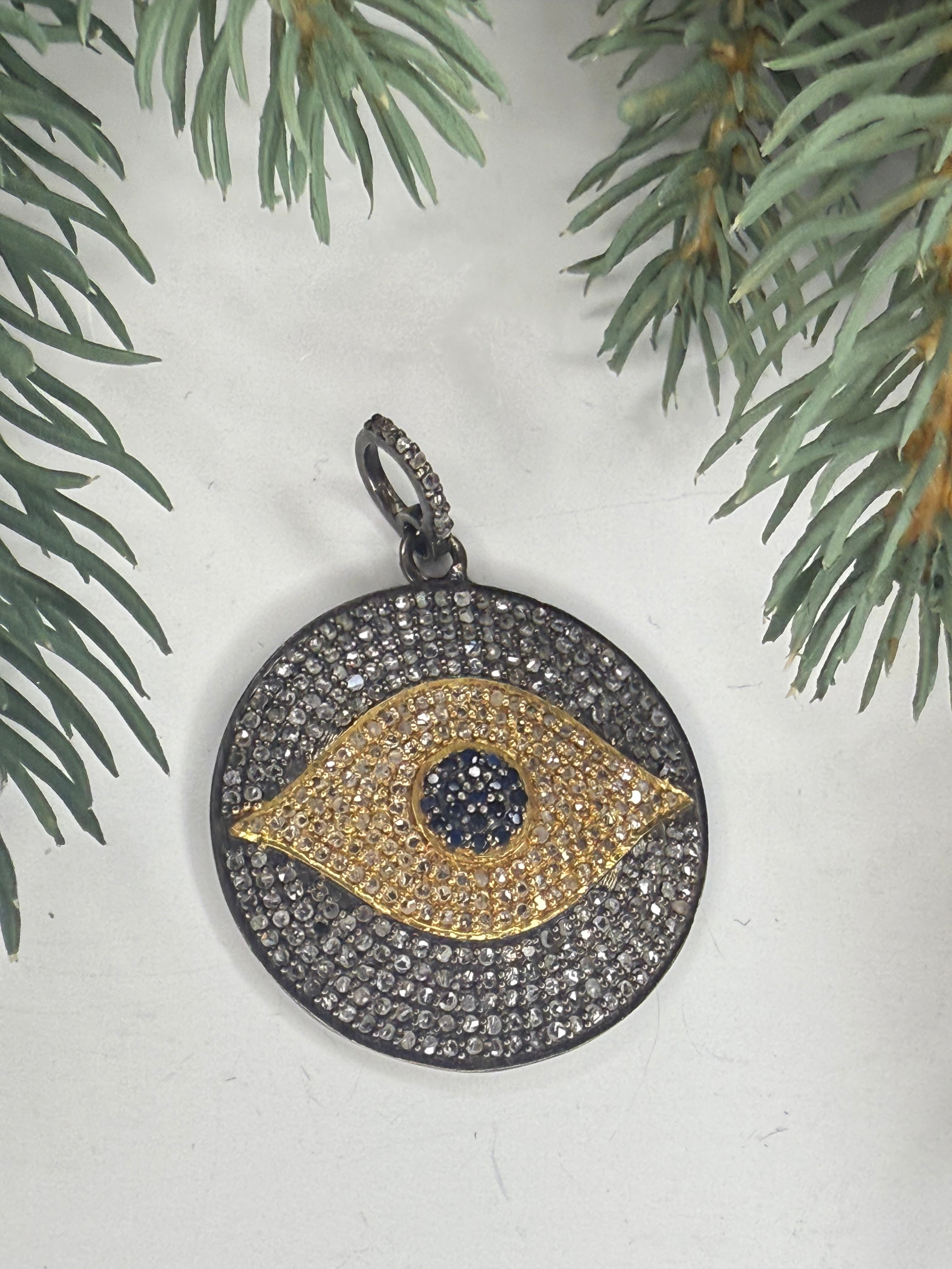 Pave diamond pendant with eye design on a white surface with greenery